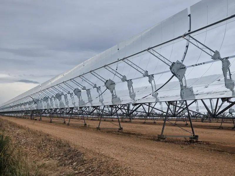 A long row of parabolic-trough CSP mirrors on steel supports beside a gravel track