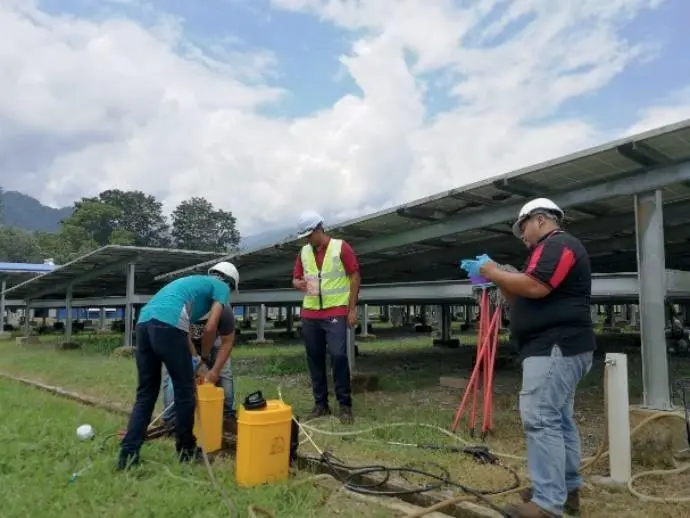 A field team in hard hats preparing yellow product containers, hoses and poles beneath a raised solar array