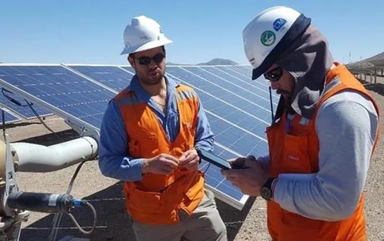 Two technicians in high-visibility vests reviewing a tablet beside a row of solar panels