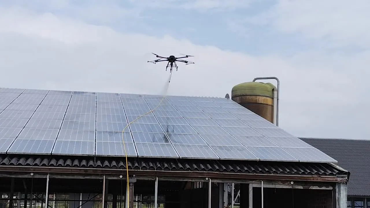 A cleaning drone spraying solar panels on a farm-shed roof, fed by a ground hose