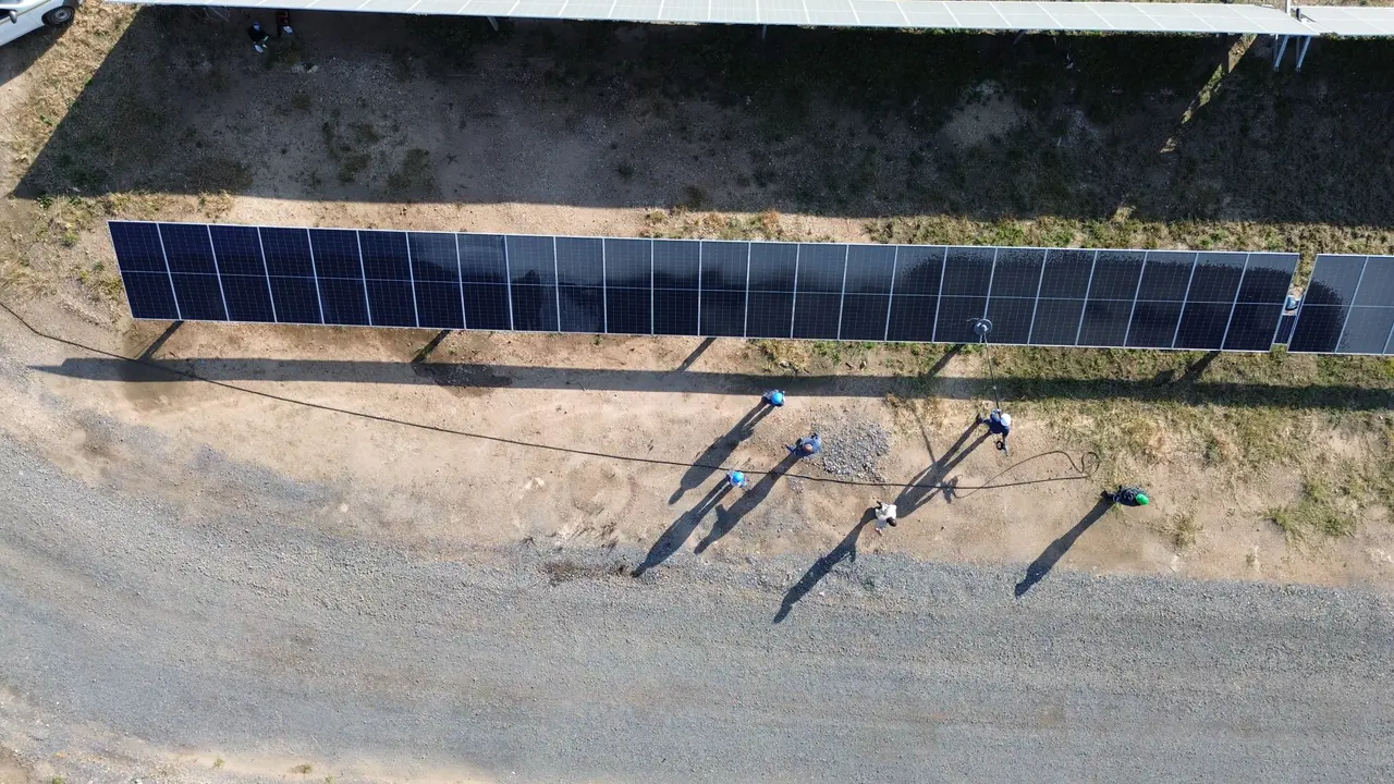 Top-down drone view of a cleaning crew with a hose working along one cleaned, dark module row